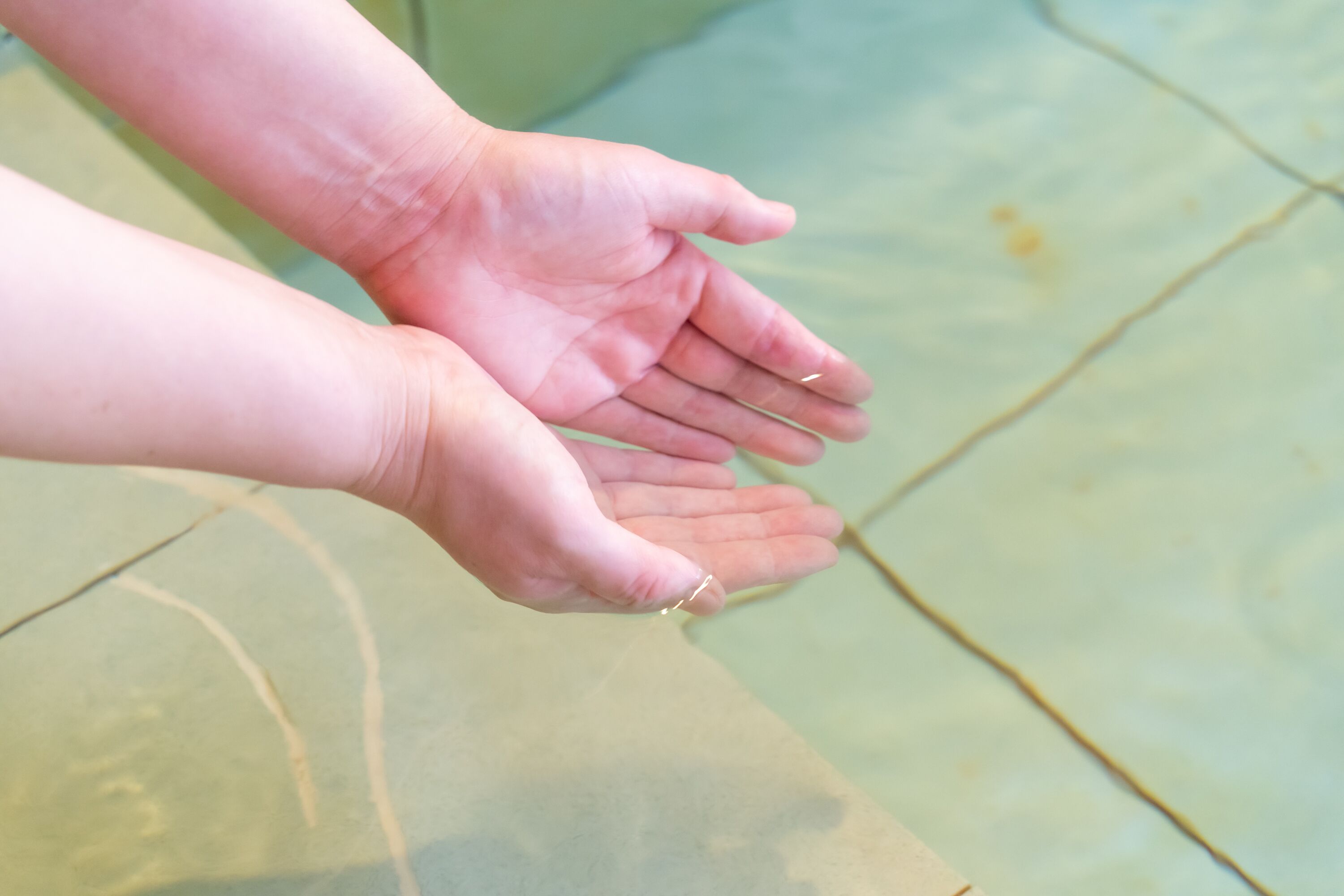 A close-up of hands reaching towards each other over a tiled floor.