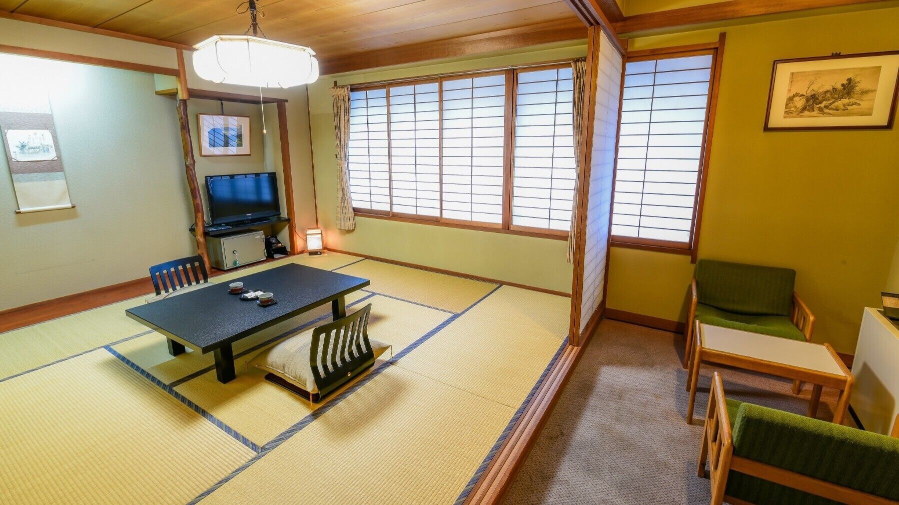 Una habitación japonesa tradicional con suelo de tatami, una mesa baja, sillas, un televisor y puertas correderas.