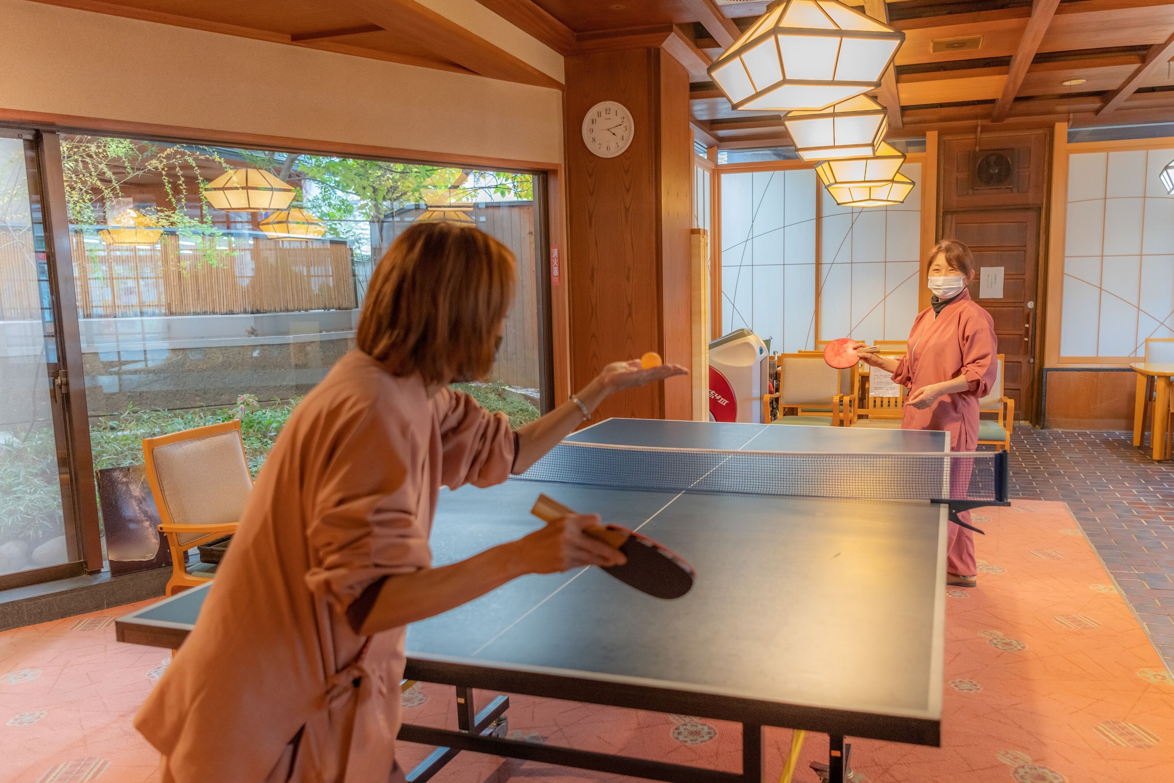 Une table de ping-pong dans une pièce aux murs en bois et aux grandes fenêtres.