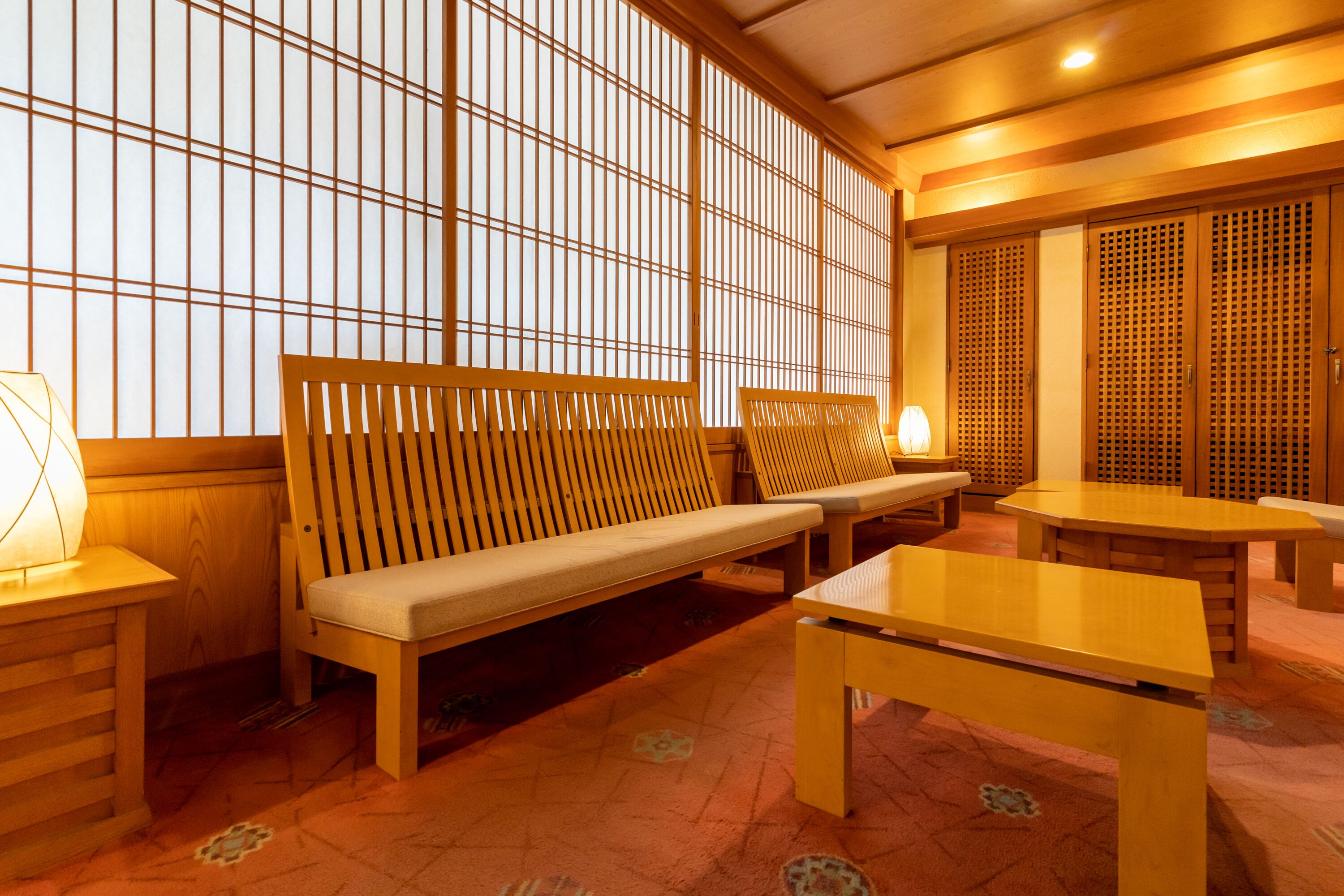 Una habitación japonesa tradicional con suelo de tatami, una mesa de madera baja, un banco acolchado y puertas correderas.