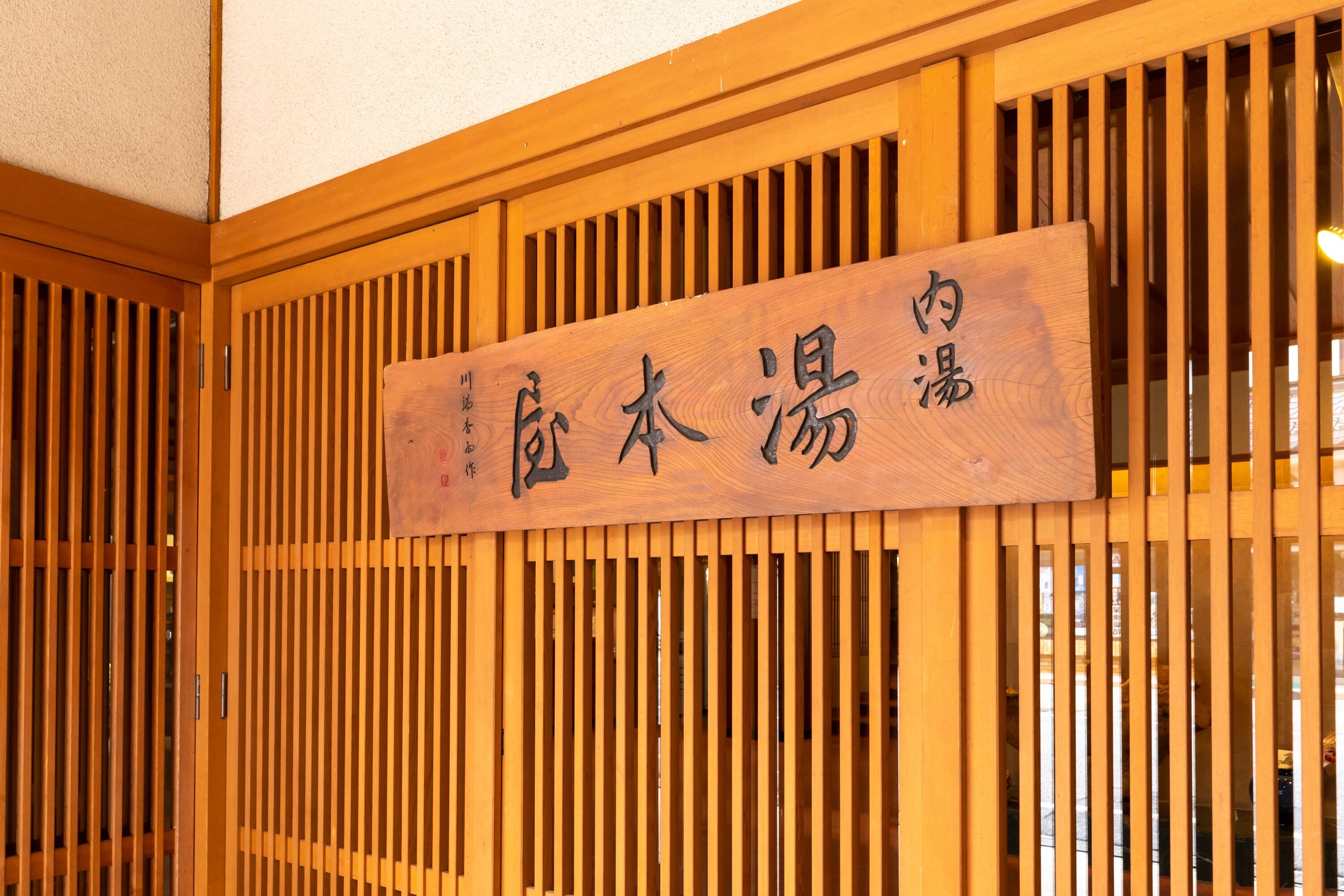 Ein hölzernes Schild mit chinesischen Schriftzeichen an einer Gebäudefassade.