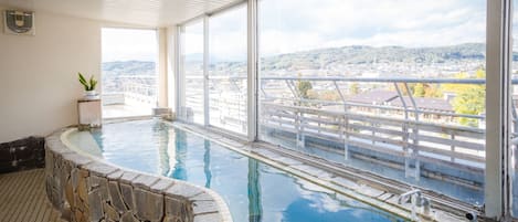 An indoor swimming pool with stone walls and a view of a cityscape through large windows.