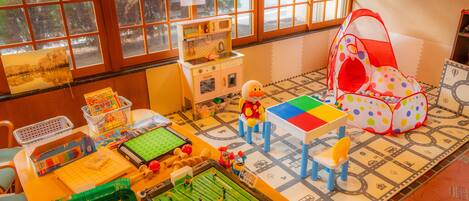 Una sala de juegos con una mesa de futbolín, una cocina de juguete y una tienda de campaña colorida.