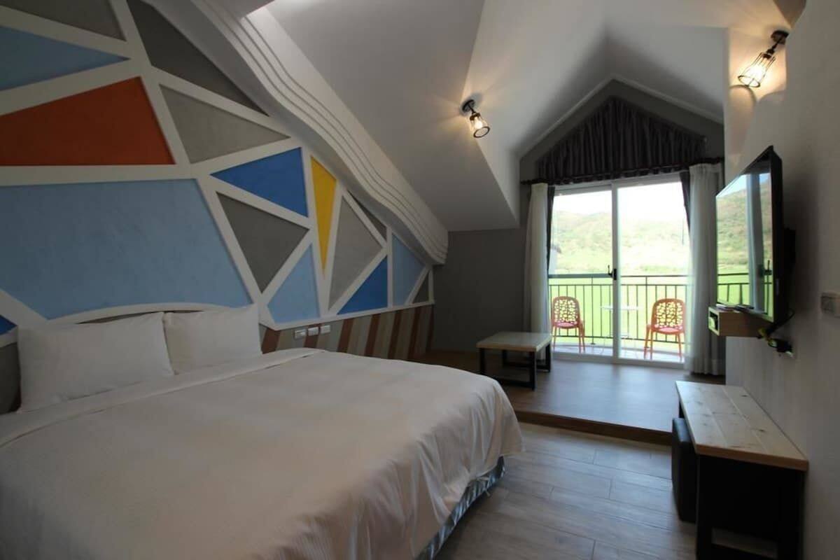 Un dormitorio con una cama grande, una mesita, un banco y un balcón con sillas.