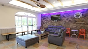 A modern lounge area with a sofa, ottoman, and two chairs. A flat-screen TV is mounted on the wall, and there is a bench along the window. - Island On The Sea (Hengchun)