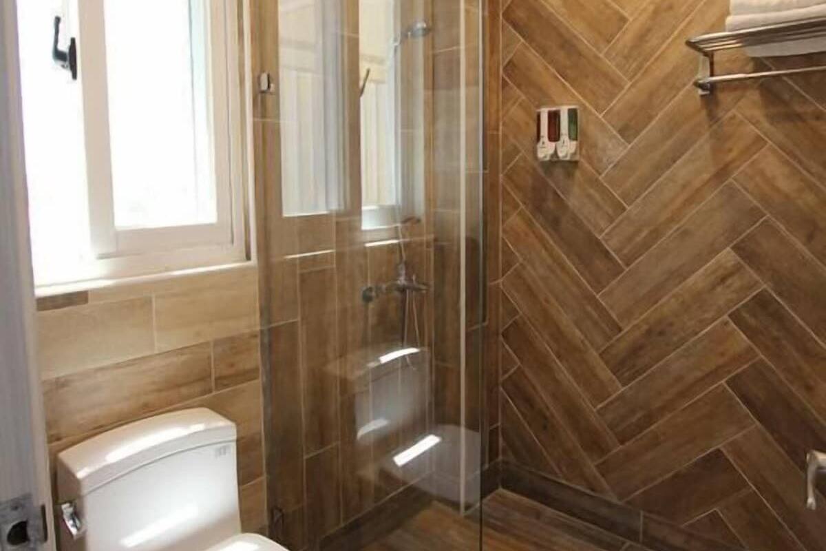 Un baño moderno con cabina de ducha de vidrio, inodoro y suelo de madera con estampado de espiga.