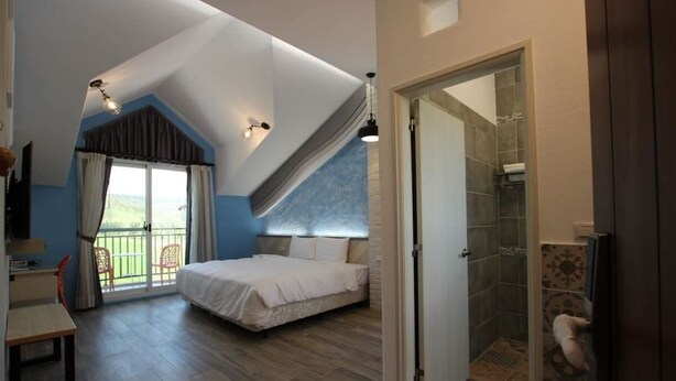 A bedroom with a bed, a desk, and a balcony with chairs. - Island On The Sea (Hengchun)