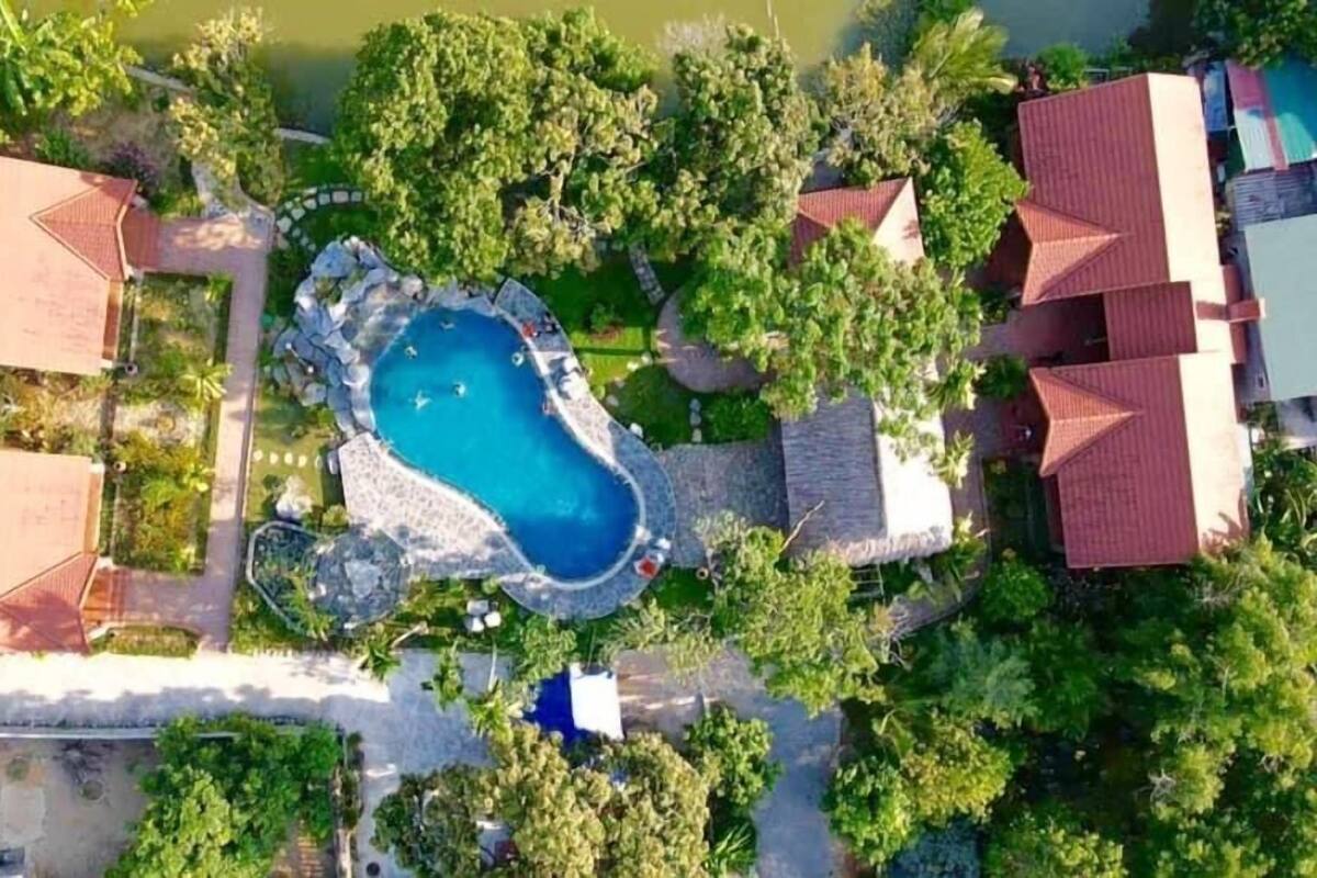 Vista aérea de una propiedad con piscina central rodeada de exuberante vegetación y varios edificios con tejados rojos.