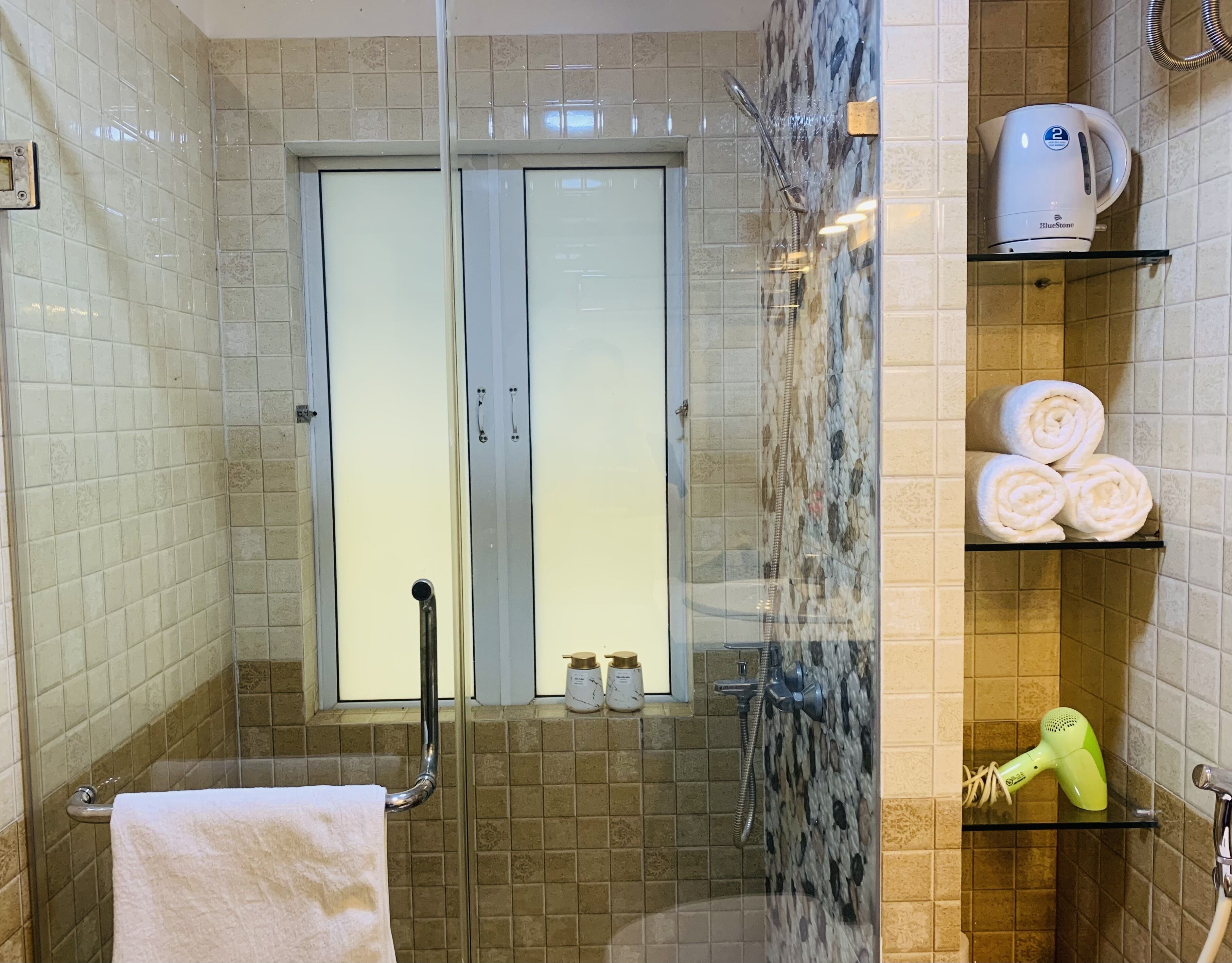 Une salle de bain avec une douche à parois de verre, un porte-serviettes, une étagère avec des serviettes pliées, un sèche-cheveux et une machine à café.