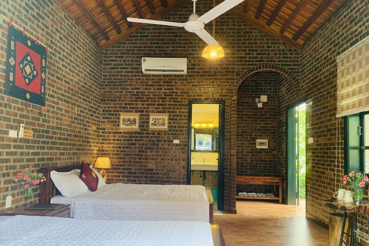 Una habitación amplia con una cama grande, ventilador de techo, pared de ladrillo y suelo de madera.