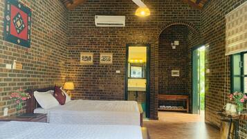 A spacious room with a large bed, a ceiling fan, a brick wall, and a wooden floor.