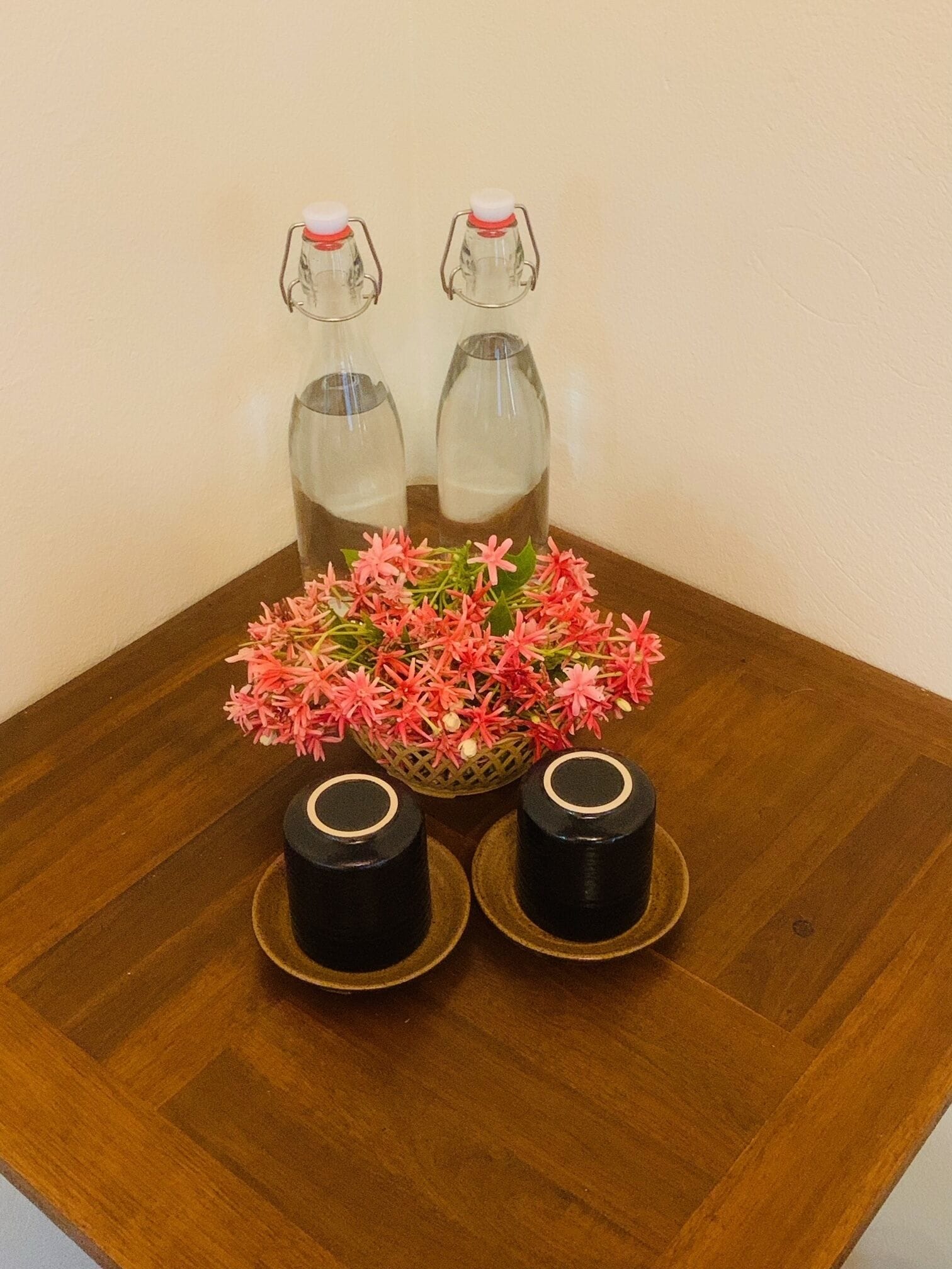 Une table en bois, deux bouteilles en verre, un panier de fleurs roses et deux récipients noirs.