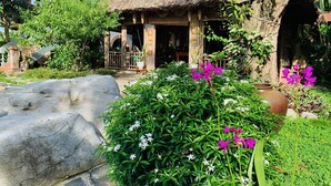 A rustic building with a thatched roof, surrounded by lush greenery and flowering plants.