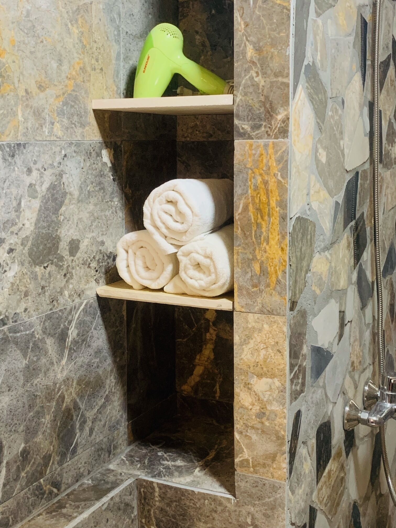 A bathroom with a shower area, a towel rack with neatly rolled towels, and a hairdryer on a shelf.