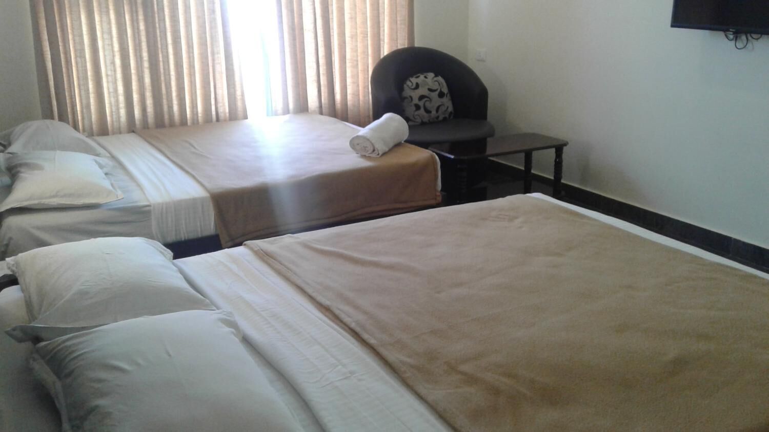 A hotel room with two beds, a chair, and a small table.