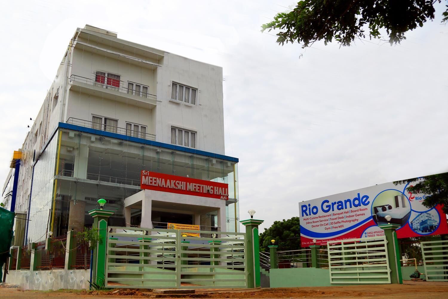 A building with a sign for Sri Meenaakshi Meeting Hall and another for Rio Grande, featuring a multi-cuisine restaurant, banquet hall, board room, 24hr room service, travel desk, indoor games, doctor on call, gym, and free WiFi.