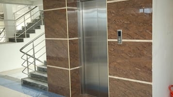 A modern elevator with a metallic finish, adjacent to a marble wall with a geometric pattern.