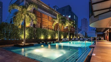 Una piscina con tumbonas y palmeras, rodeada de edificios de arquitectura moderna.