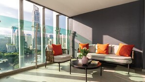 A modern living room with a sofa and armchair, a coffee table, and a view of a cityscape through large windows. - Solitaire Bangkok Sukhumvit 11 by Kingston Hotels (Bangkok)
