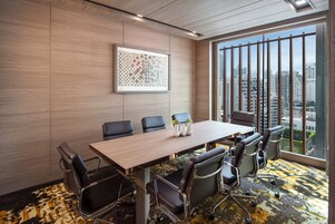 A conference room with a large table, six chairs, a framed artwork on the wall, and a city view through large windows.