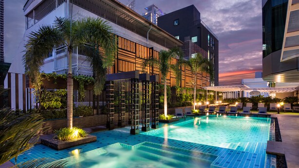 A swimming pool with lounge chairs and palm trees, surrounded by modern buildings. - Solitaire Bangkok Sukhumvit 11 by Kingston Hotels (Bangkok)