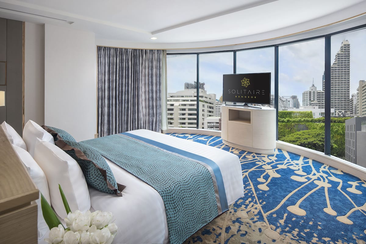 A modern hotel room with a large bed, a television, and a city view.