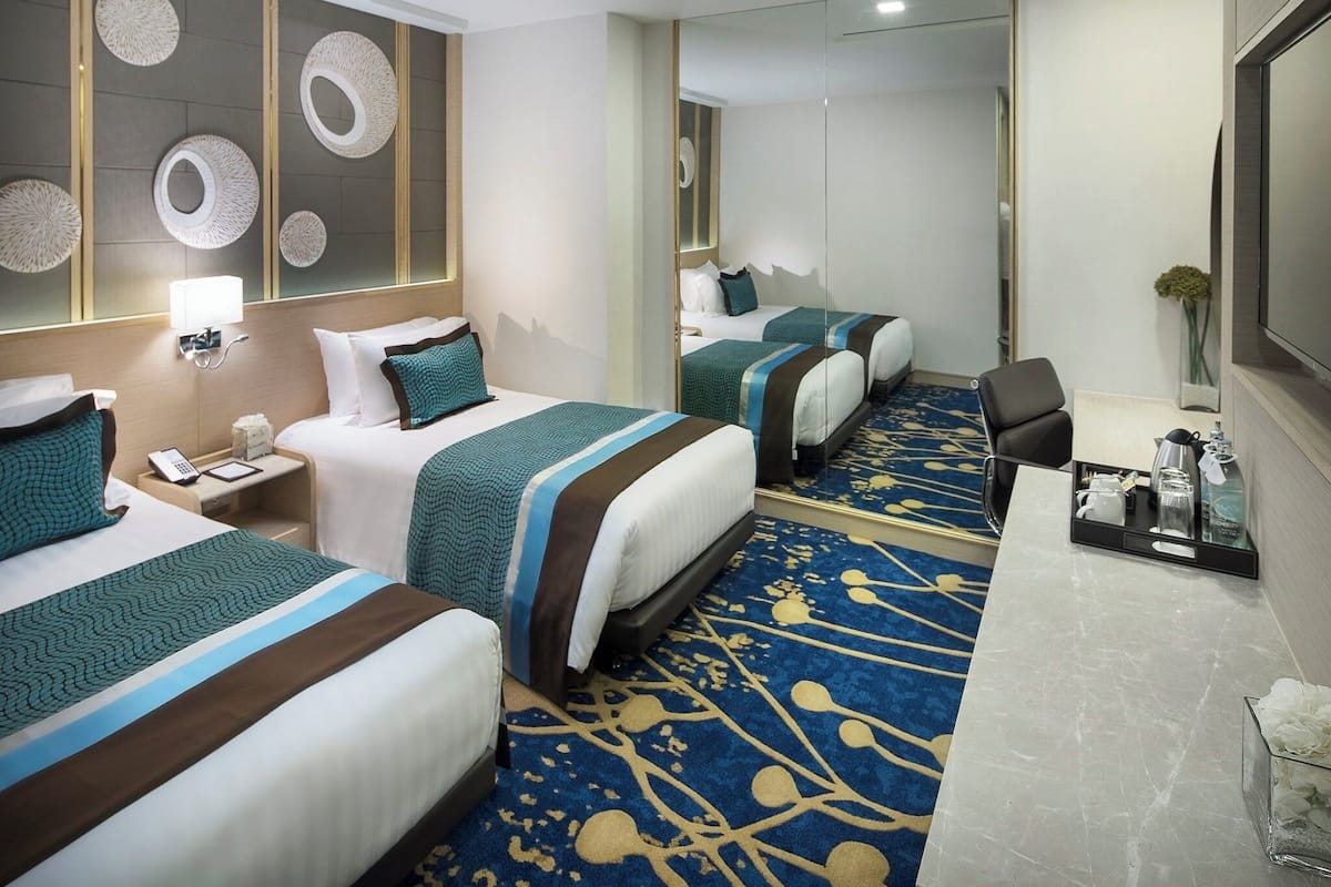 A hotel room with two beds, a desk, a mirror, and a decorative wall.