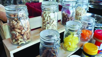 On peut voir une variété de bocaux en verre contenant différents aliments, comme des noix, des fruits secs et des légumes, disposés sur une étagère en bois.