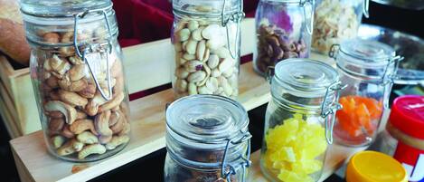 A variety of glass jars containing different food items like nuts, dried fruits, and vegetables on a wooden shelf.