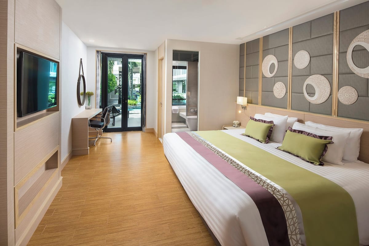 A modern hotel room with a large bed, a desk, a TV, and a view of the outdoors.