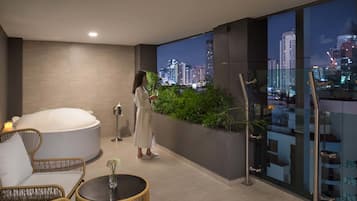 A modern room with a large bathtub, a glass wall with a city view, and a small table with a vase.