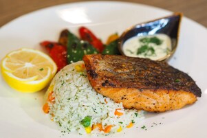 A plate with grilled salmon, rice, mixed vegetables, and a lemon wedge.