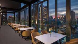 A rooftop restaurant with tables and wicker chairs, offering a city view. - Solitaire Bangkok Sukhumvit 11 by Kingston Hotels (Bangkok)