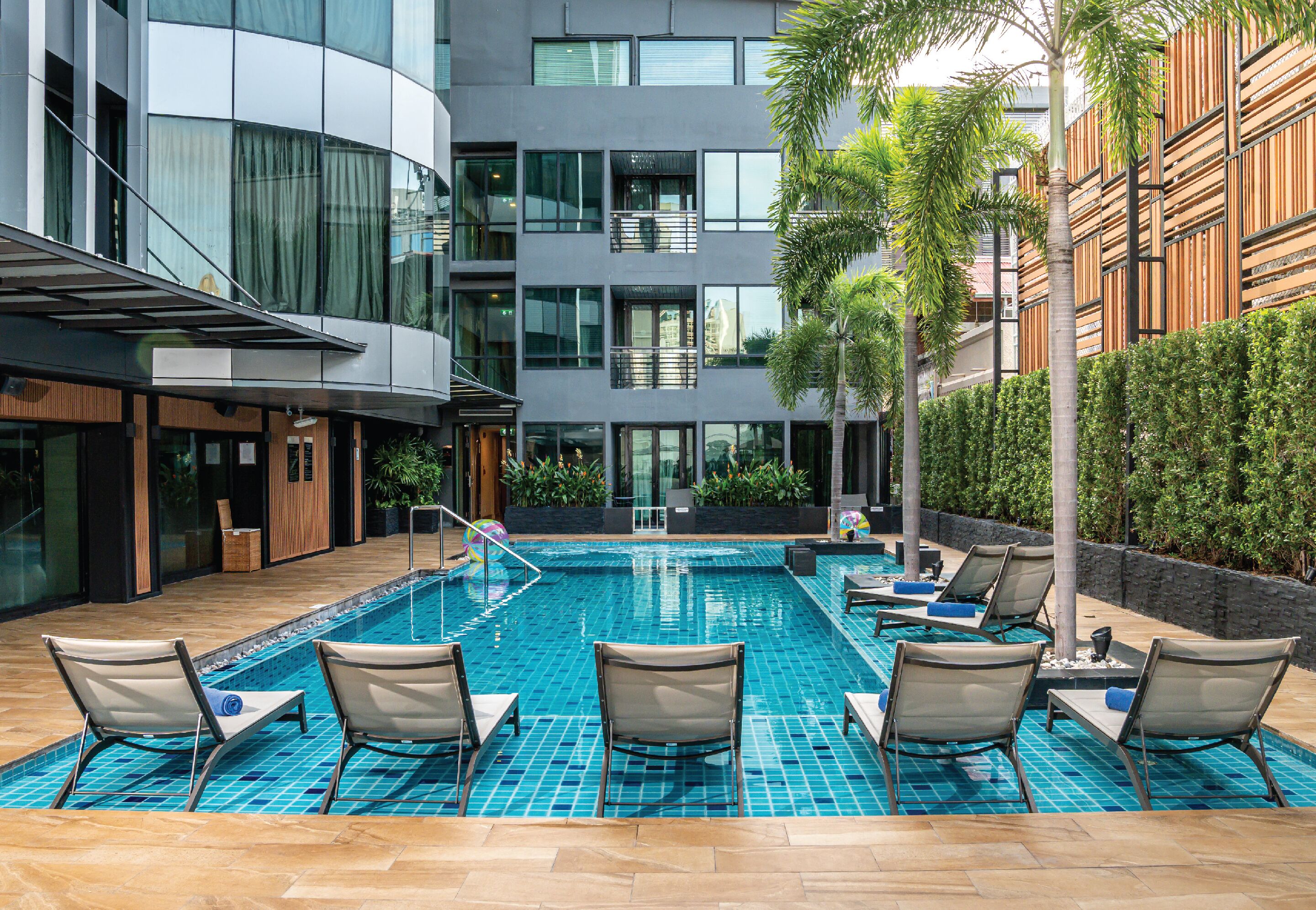 Um hotel moderno com piscina, espreguiçadeiras e vista para a cidade.