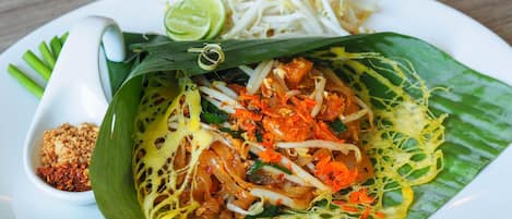 A plate of Pad Thai with bean sprouts and lime, served on a white plate with a small bowl of chili and peanuts.