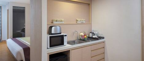 Habitación de hotel compacta con kitchenette, una cama con colcha blanca y granate, un refrigerador pequeño y un microondas.