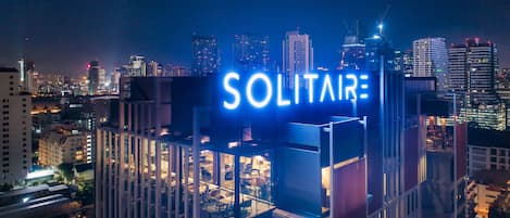 A high-rise building with a prominent 'SOLITAIRE' sign, surrounded by other tall buildings and city lights.
