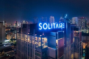 Ein Hochhaus mit einem markanten 'SOLITAIRE'-Schild, umgeben von weiteren hohen Gebäuden und Stadtlichtern.