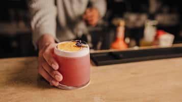 A hand holding a glass with a pink beverage and a slice of orange on the rim.