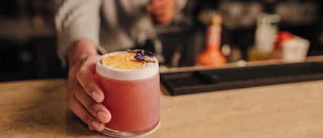 A hand holding a glass with a pink beverage and a slice of orange on the rim.