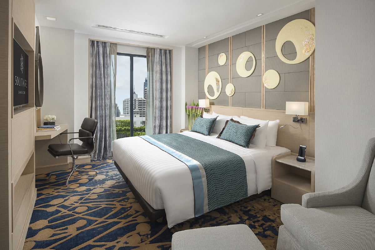 A hotel room with a large bed, a desk, a chair, and a view of the city.