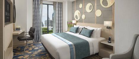 A hotel room with a large bed, a desk, a chair, and a view of the city.