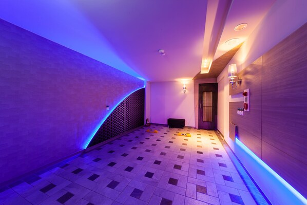 A hallway with a checkered floor, a curved wall with blue lighting, and a bench. - TY Motel (Taoyuan City)
