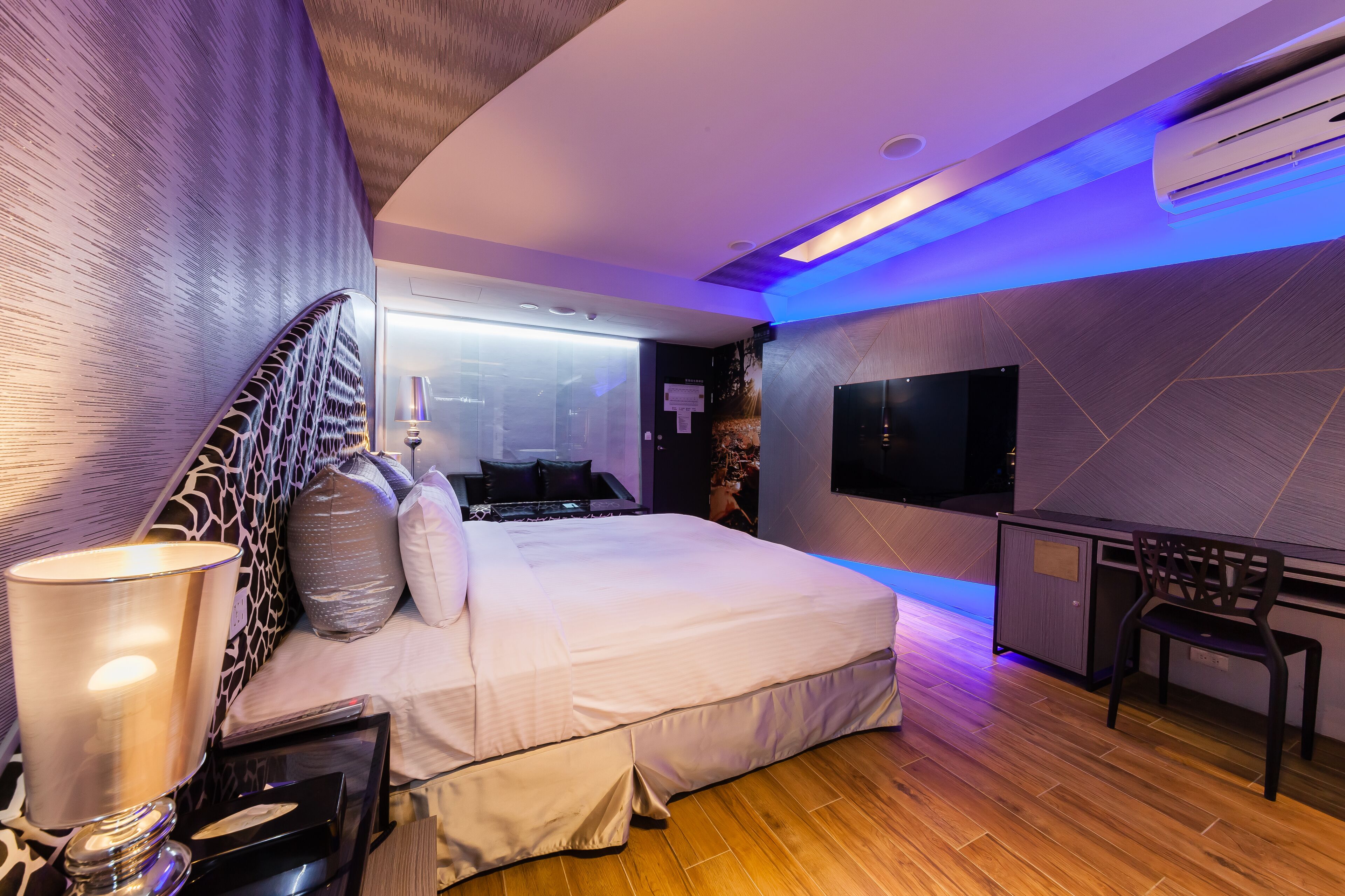 A modern hotel room with a large bed, a desk, and a flat-screen TV.