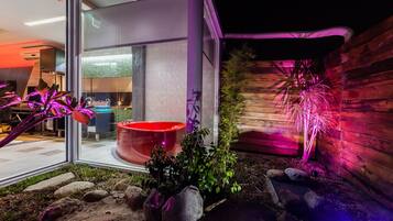 A modern outdoor area with a glass enclosure, a red planter, and a wooden wall with a decorative light.