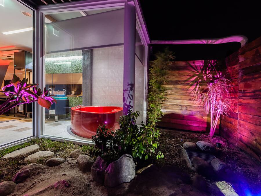 A modern outdoor area with a glass enclosure, a red planter, and a wooden wall with a decorative light.
