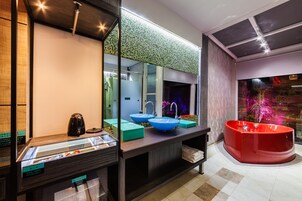 Un baño moderno con un espejo grande, dos lavamanos, una bañera roja y un expositor de vidrio.