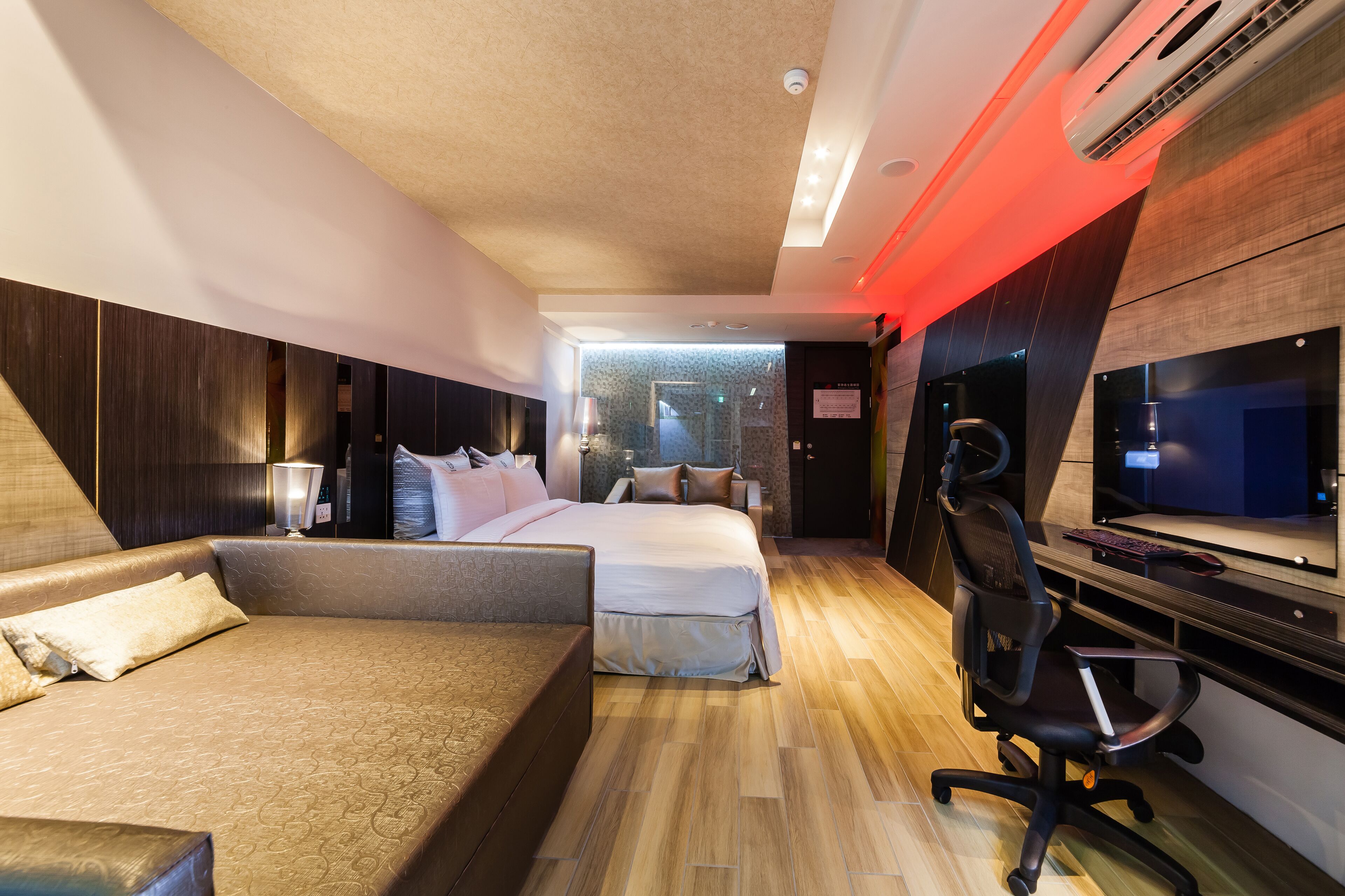 Habitació d'hotel moderna amb un llit gran, un sofà, una taula de treball amb un ordinador i una televisió.