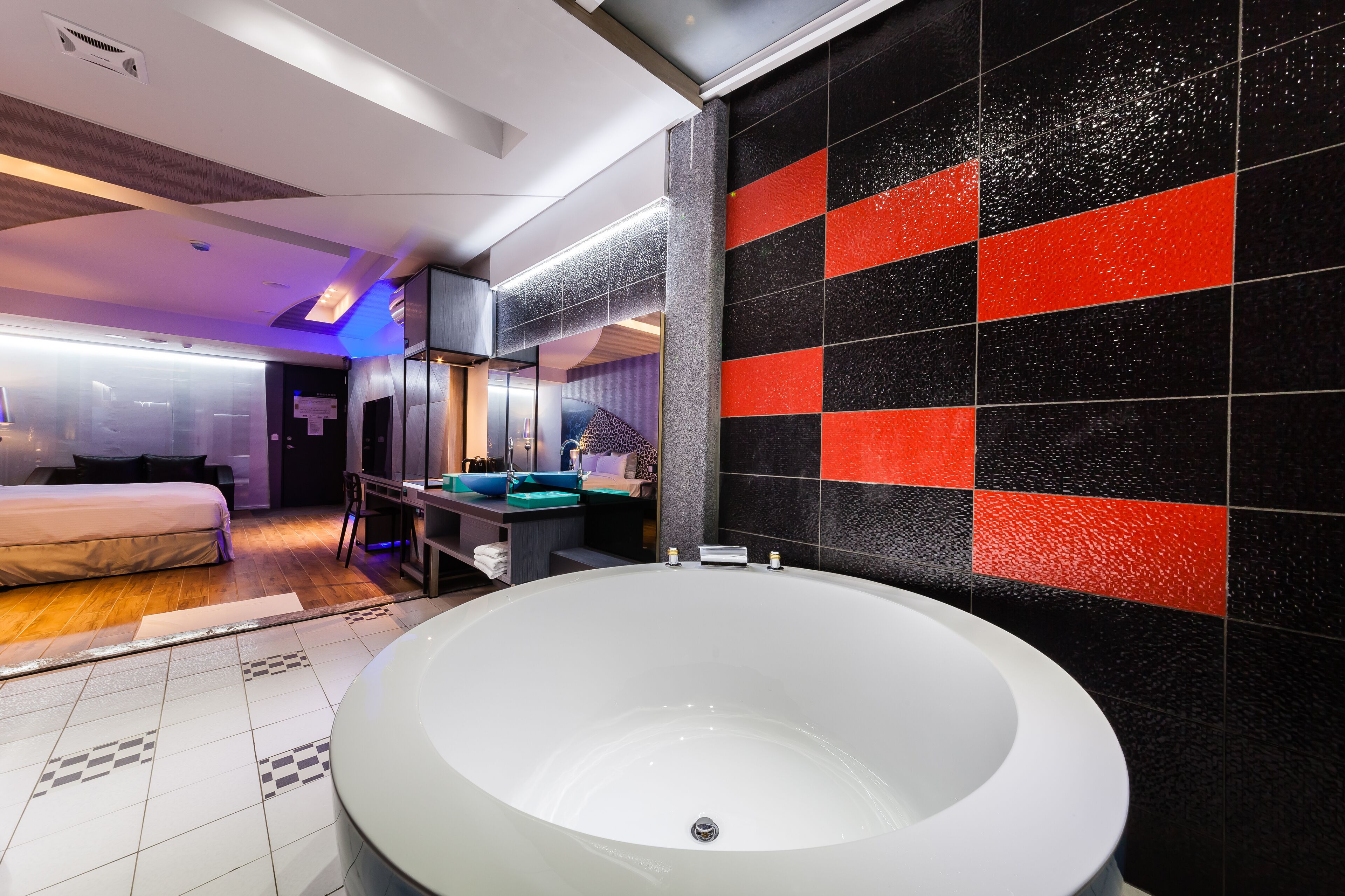 Une chambre d’hôtel moderne dotée d’une grande baignoire, d’une salle de bain séparée avec un lavabo bleu et d’un lit offrant une vue sur la ville.