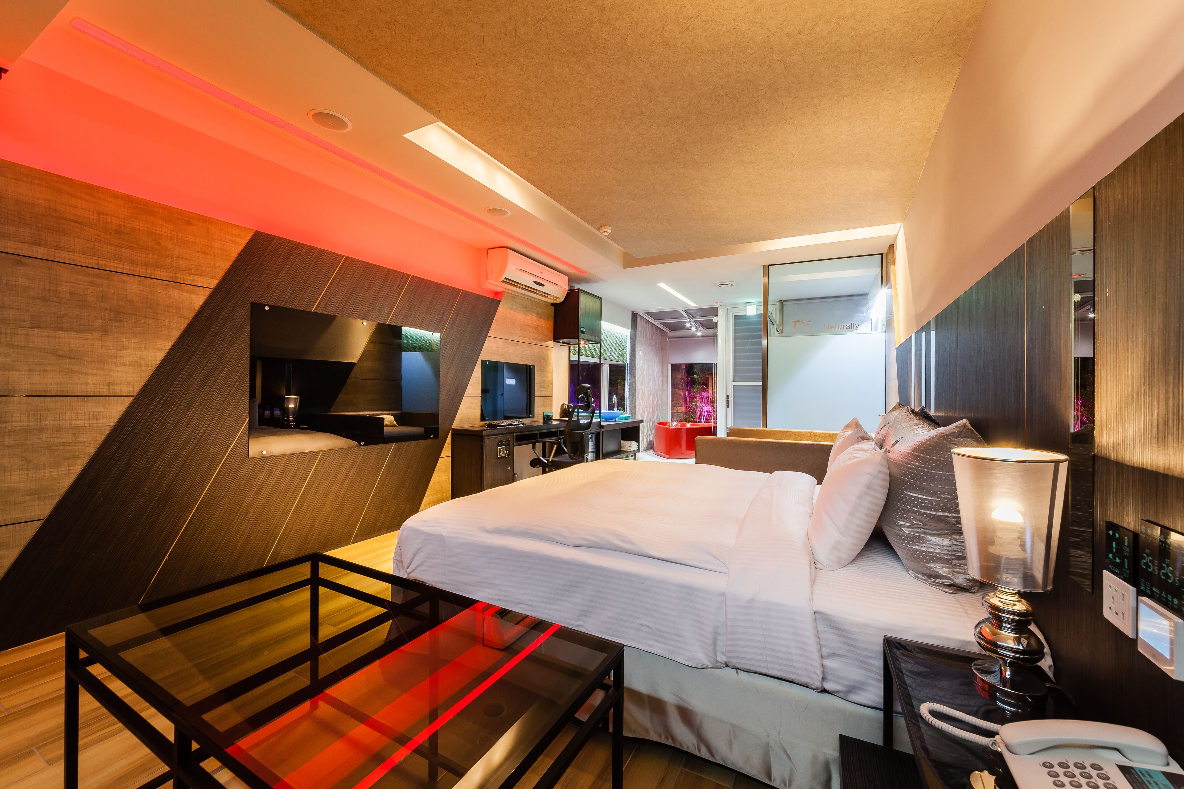 Een moderne hotelkamer met een bed, nachtkastje, bureau en een groot raam.